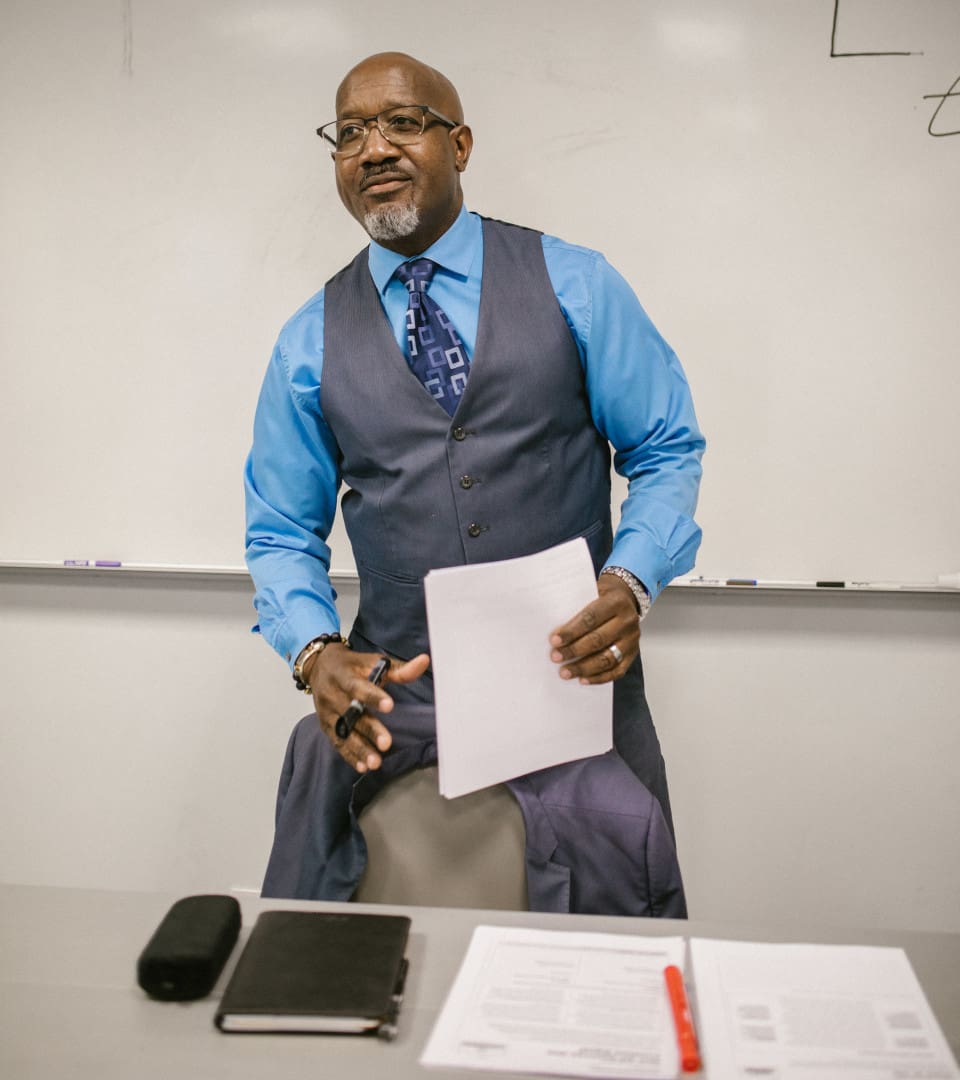 A man in a blue shirt and vest holding papers.