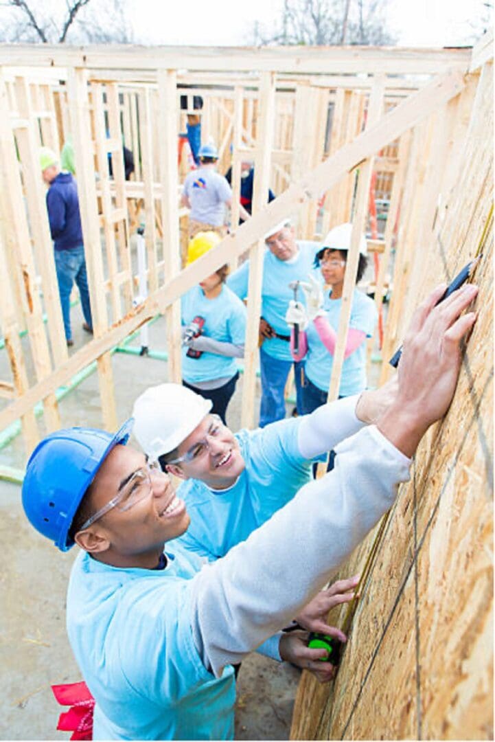 A group of people in hard hats and blue shirts working on walls.